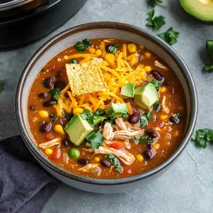 Eine Schüssel herzhafte Suppe mit zerrupftem Hähnchen, schwarzen Bohnen, Mais, Avocadowürfeln, Cheddar und Tortilla-Chips, garniert mit Koriander.