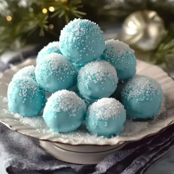 Ein Teller mit hellblauen Pralinenkugeln in Zucker gewälzt, wie eine verschneite Anordnung, umgeben von weihnachtlichem Grün.