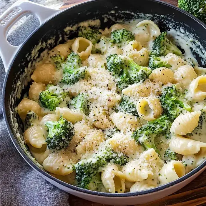 Ein cremiges Pastagericht mit Brokkoli und muschelförmigen Nudeln, bestreut mit geriebenem Käse und schwarzem Pfeffer in einem Kochtopf.