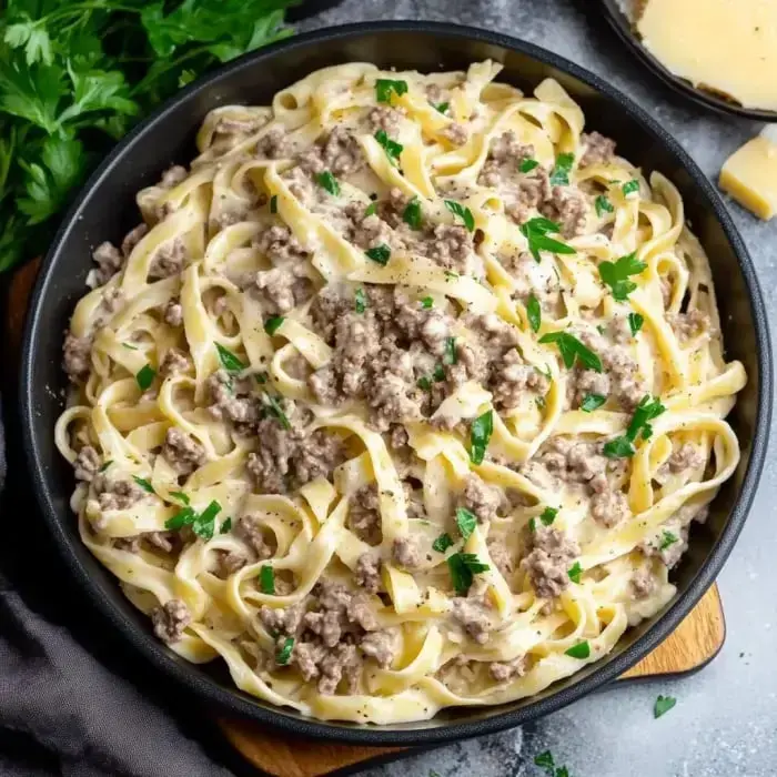 Eine Schüssel cremige Fettuccine-Pasta mit gewürztem Hackfleisch und frischer Petersilie garniert.