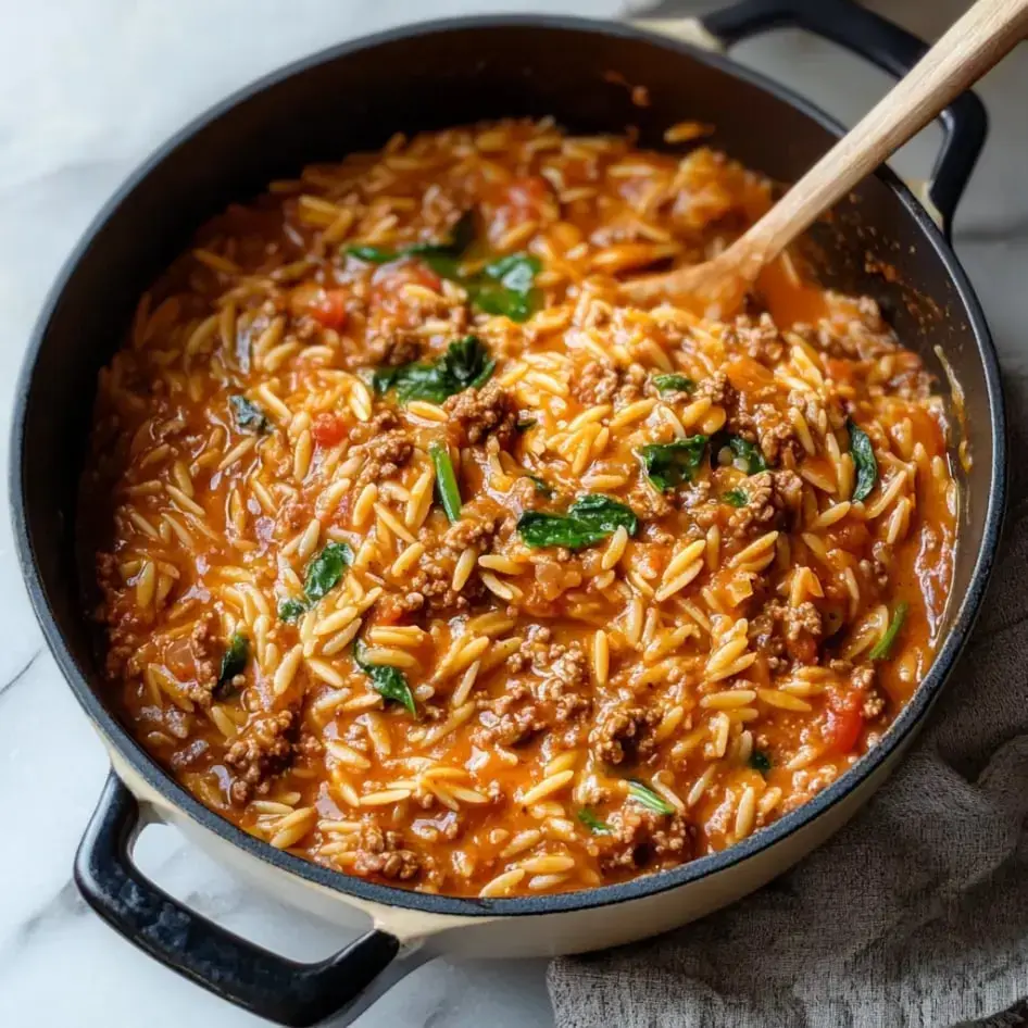 Ein Topf mit cremiger Orzo-Pasta, gemischt mit Hackfleisch, Spinat und gewürfelten Tomaten.