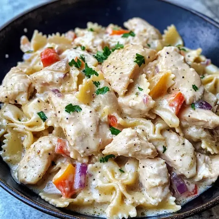 Eine Schüssel cremige Pasta mit Hähnchen, Paprikaschoten und mit Petersilie garniert.