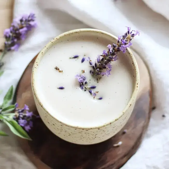 Eine Aufsicht auf ein cremiges Getränk, garniert mit frischen Lavendelblüten in einer gesprenkelten Keramiktasse, ruhend auf einer Holzoberfläche.