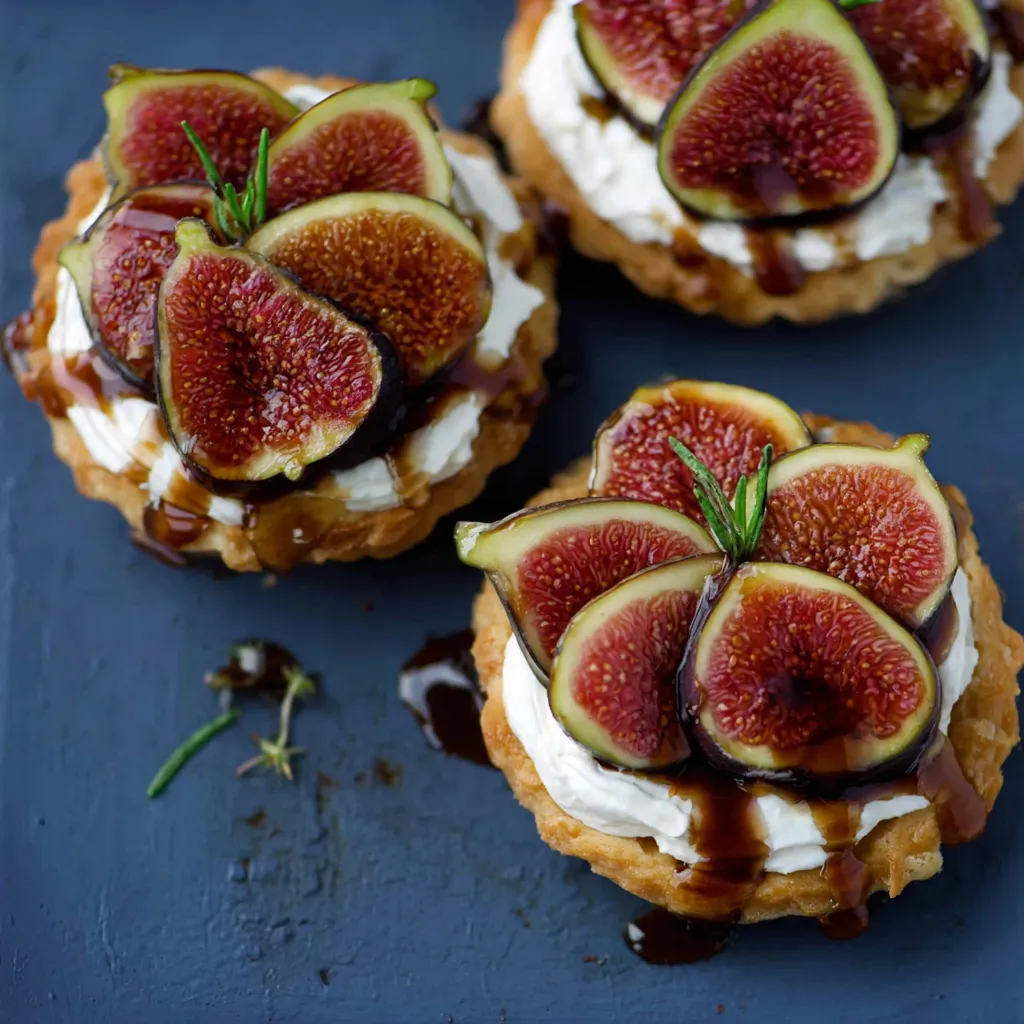 Zwei kleine, frische Fruchtkuchen mit Fruchtgarnituren und Sahne auf einem Tisch.