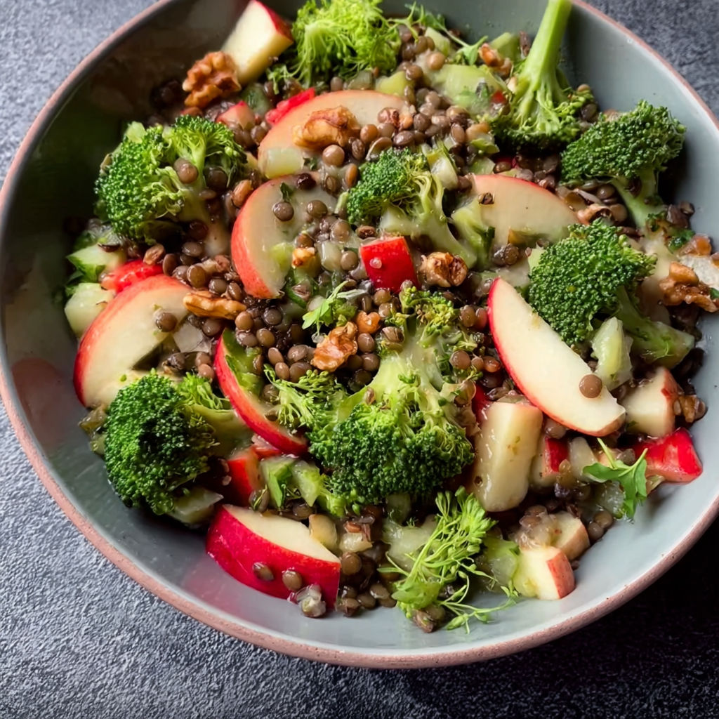 A bowl of food with broccoli, apples, and other vegetables.