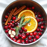 Ein Topf gefüllt mit Cranberries, Orangenscheiben, Zimtstangen und Rosmarin in Wasser schwimmend.