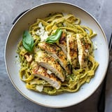 Eine Schüssel Fettuccine-Pasta belegt mit geschnittenem gegrilltem Hähnchen, Basilikum und Pesto-Sauce, garniert mit geriebenem Käse.