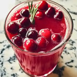 Ein Glas leuchtend roter Cranberrysaft ist mit frischen Cranberries gefüllt und mit einem Rosmarinzweig garniert.