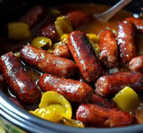 Eine Nahaufnahme von gekochten Würstchen mit gelben Paprika in einer reichhaltigen Sauce im Slowcooker.