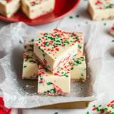 Ein Stapel festlicher weißer Fudge-Würfel, verziert mit roten und grünen Streuseln auf einem goldenen Tablett.