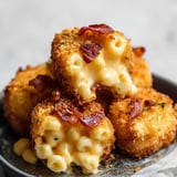 Knusprige, goldbraune Mac and Cheese Bites mit Speckstückchen sind auf einem Teller gestapelt und zeigen geschmolzenen Käse und Makkaroni im Inneren.