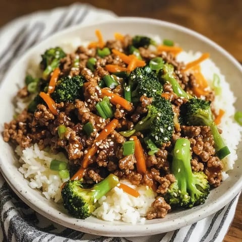 Eine Schüssel Reis belegt mit gebratenem Hackfleisch, Brokkoli, Karotten und Frühlingszwiebeln, garniert mit Sesamsamen.