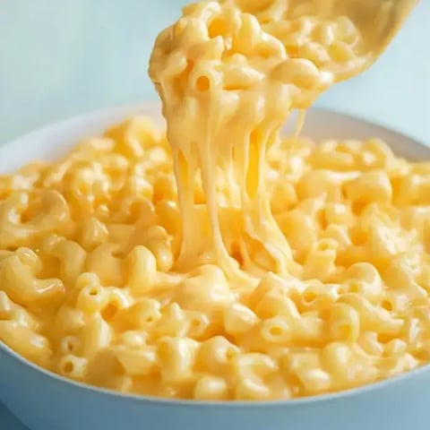 Ein Löffel hebt cremige Makkaroni mit Käse aus einer Schüssel und zeigt ihre reichhaltige, geschmeidige Textur.