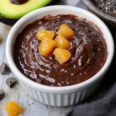 Ein Glas mit einer schwarzen Sauce, die mit einer Avocado und einer Orange garniert ist.