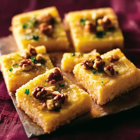 Ein Teller mit sechs quadratischen, weißen, mit Walnüssen und Zwiebeln garnierten Cakes.
