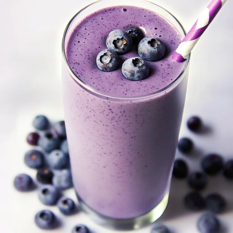 Ein Glas mit Blaubeeren-Smoothie, der in einem Glas mit einem Strohhalm gefüllt ist.