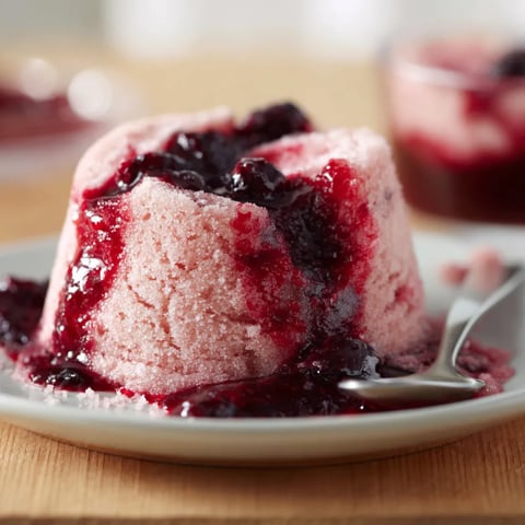 Eine Tasse mit einem Dessert, das aus einer Masse von Zuckar, Sahne und Beeren besteht.