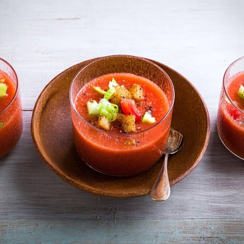Ein Glas mit einer roten Suppe, die mit Zwiebeln und Tomaten garniert ist.