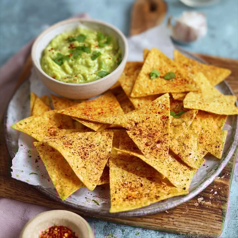A plate of tortilla chips with a bowl of guacamole.