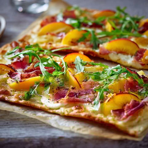 A pizza with peaches and bacon on it.