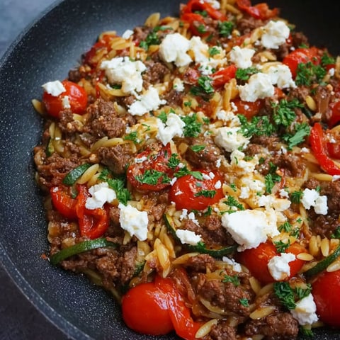 A bowl of food with tomatoes, cheese, and noodles.